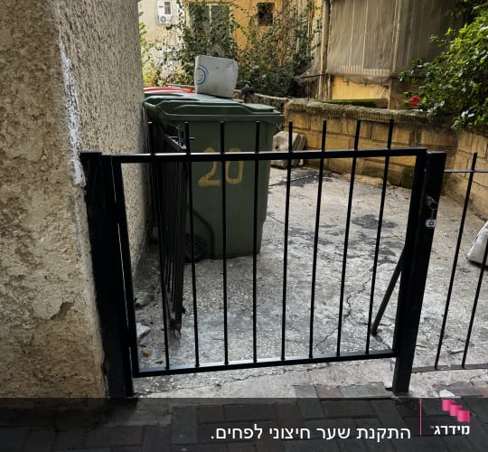 שער מתכת קטן ליד פח אשפה בחצר